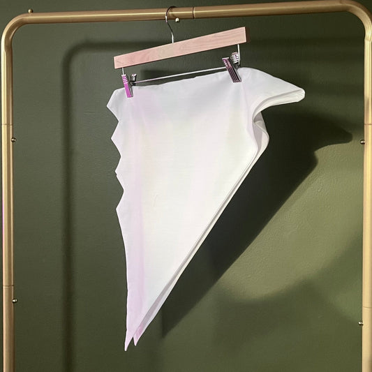 A white triangular head tie with a zig zag edge, hanging from a wooden hanger on a gold-colored clothing rack against a dark olive green wall.